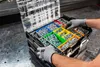 A person wearing gloves is sorting screws and bolts into a multi-compartment organizer box. Produktbild-Vorschau