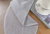 A close-up of a gray linen-look fabric with a white cup and saucer on a book in the background. Produktbild-Vorschau