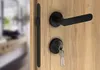 A close-up view of a black door handle and lock mechanism on a wooden door. Produktbild-Vorschau
