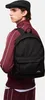 A man wearing a black flat cap and a maroon tracksuit with white stripes, carrying a black backpack. Produktbild-Vorschau