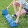 A person is kneeling on grass, partially unfolding a blue ground tarp for a pool. Produktbild-Vorschau