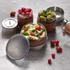 Three stacked lunch containers filled with food, along with scattered strawberries and tomatoes, on a gray surface. Podgląd zdjęcia produktu