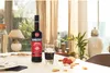 A bottle of Ramazzotti Amaro and a glass of the drink are placed on a table with cookies and strawberries, in a well-lit room with curtains and decorative vases in the background. Produktbild-Vorschau
