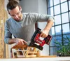 A man is using a cordless nail gun to assemble a wooden birdhouse indoors. Produktbild-Vorschau