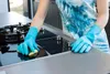 A person wearing blue gloves is cleaning a black glass stovetop with a yellow sponge. Náhľad obrázku produktu