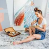 An artist is sitting on the floor in her studio, painting. Anteprima dell’immagine prodotto
