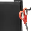 A close-up shot of a black monitor hook holding a pair of orange-handled scissors. Produktbild-Vorschau