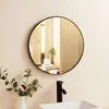 A round mirror hangs on a wall above a sink and faucet in a bathroom. Produktbild-Vorschau