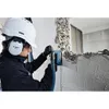 A person wearing safety gear is using a Bosch angle grinder with a dust extraction hood attached to cut into a wall. Voir les images du produit