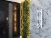 A modern bathroom with a black marble shower wall, a vertical green plant wall, and a white towel radiator on a gray marble wall. Podgląd zdjęcia produktu