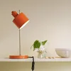 A modern orange desk lamp is displayed on a white shelf. Produktbild-Vorschau