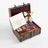 An open trunk filled with small items resembling books, with a letter and a decorative butterfly-like object. Produktbild-Vorschau