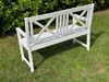 A white wooden garden bench sits on a grassy lawn with a green hedge in the background. Produktbild-Vorschau