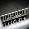 A close-up shot of a metal grate with rectangular openings, showing some damage in one of the openings. Below the grate are several metal prongs. Náhľad obrázku produktu