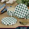 A collection of green and white checkered jar lids on a wooden surface, with some mushrooms and herbs in the background. Produktbild-Vorschau