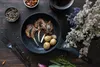 A rustic overhead shot of a pan with lamb chops, potatoes, and garlic, surrounded by spices and herbs, with a bouquet of dried flowers in the background. Produktbild-Vorschau