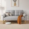 A light gray sofa with throw pillows and a blanket is shown in a well-lit room with a wooden floor and a rug. Produktbild-Vorschau