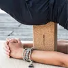A person's hands and legs are shown in a yoga pose, with a cork yoga block supporting their legs. They are wearing a mala bracelet. Produktbild-Vorschau
