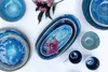 A collection of blue ceramic dishes and mugs arranged on a white surface, with a sprig of pink flowers. Produktbild-Vorschau