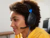 A young person wearing a yellow hoodie and black and blue gaming headphones. Produktbild-Vorschau