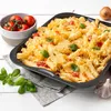 A close-up shot of a baked pasta dish in a black baking pan, with fresh tomatoes, basil, and garlic as garnishes. Anteprima dell’immagine prodotto