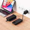 A tablet and two power banks are on a wooden desk, with one power bank plugged into a wall outlet. Anteprima dell’immagine prodotto