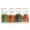 Four glass spice jars with clear lids, each containing a different spice, arranged in a row on a white background. Voir les images du produit
