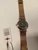 The back of a rose gold watch with a mesh strap is shown, along with its tag. Produktbild-Vorschau