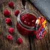 A jar of raspberry jam and loose raspberries on a wooden surface. Podgląd zdjęcia produktu