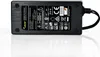 A black power adapter with a label showing product information and certifications, placed on a reflective white surface. Produktbild-Vorschau