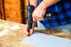 A person is using a cordless drill to attach a hinge to a piece of wood. Podgląd zdjęcia produktu