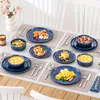 A table setting with a full dinnerware set, including plates, bowls, and cutlery, arranged with various food items. Produktbild-Vorschau