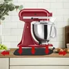 A red stand mixer is shown on a kitchen counter with a mat underneath it. There are grapes on the left and croissants on the right. Produktbild-Vorschau
