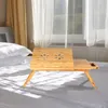 A bamboo laptop table with a drawer is set up on a bed in front of a window with sheer curtains. Produktbild-Vorschau