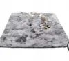 A fluffy gray rug is laid out on a white background, with decorative string lights, a small radio, and a magazine placed on it. Produktbild-Vorschau