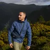 A man wearing a blue jacket and khaki pants walking in a mountainous area with yellow and green foliage. Produktbild-Vorschau