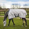 A grey horse wearing a silver Bucas Sun Shower outdoordecke is grazing in a grassy field with a wooden fence and trees in the background. Voir les images du produit