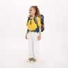 A young girl wearing a backpack stands against a white background. Voir les images du produit
