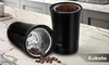 A black coffee grinder is shown on a marble countertop with coffee beans and ground coffee. Podgląd zdjęcia produktu