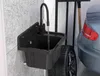 A black sink with a faucet is mounted on a gray tiled wall in a garage, next to a car tire and a car. Náhled obrázku produktu