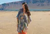 A woman stands on a sandy beach in front of the ocean and a rocky mountain. Produktbild-Vorschau