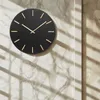 A black wall clock with gold markers is mounted on a marble-effect wall, with striped shadows cast across it. Voir les images du produit