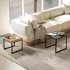 A modern living room setup with a sectional sofa, a plaid blanket draped over it, and two small side tables. One table holds a laptop and mug, while the other displays a newspaper and a bowl of nuts. A textured rug covers the floor. Náhľad obrázku produktu