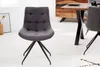 A gray upholstered dining chair with a black metal base is shown in a room with a wooden dining table and cabinet in the background. Produktbild-Vorschau