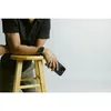 A person leaning on a stool, holding a phone. Anteprima dell’immagine prodotto