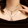 A close-up shot of a person wearing two silver necklaces with charms. Anteprima dell’immagine prodotto