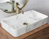 A rectangular washbasin with a marble-like pattern and gold fixtures is shown on a wooden countertop. Anteprima dell’immagine prodotto