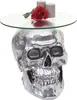 A silver skull-shaped side table with a glass top, a red rose, and two gray candles on it. Podgląd zdjęcia produktu