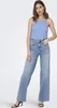 A woman is posing in a studio setting wearing a blue top and light wash wide-leg jeans. Produktbild-Vorschau