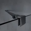 A close-up, angled view of a black shower screen hinge and support rod against a textured gray wall. Voir les images du produit